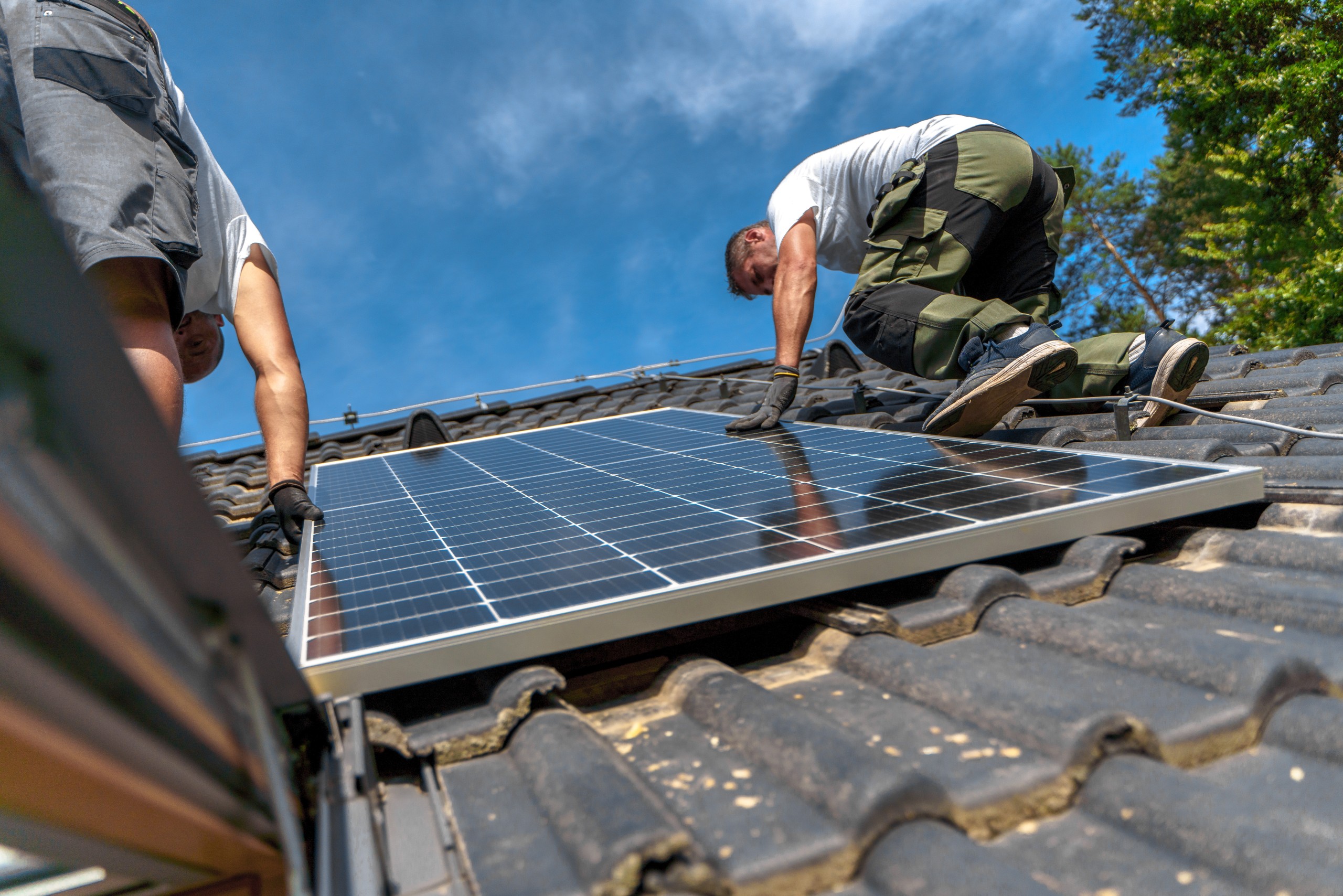 Drei Personen arbeiten auf dem Dach und montieren eine Solaranlage.